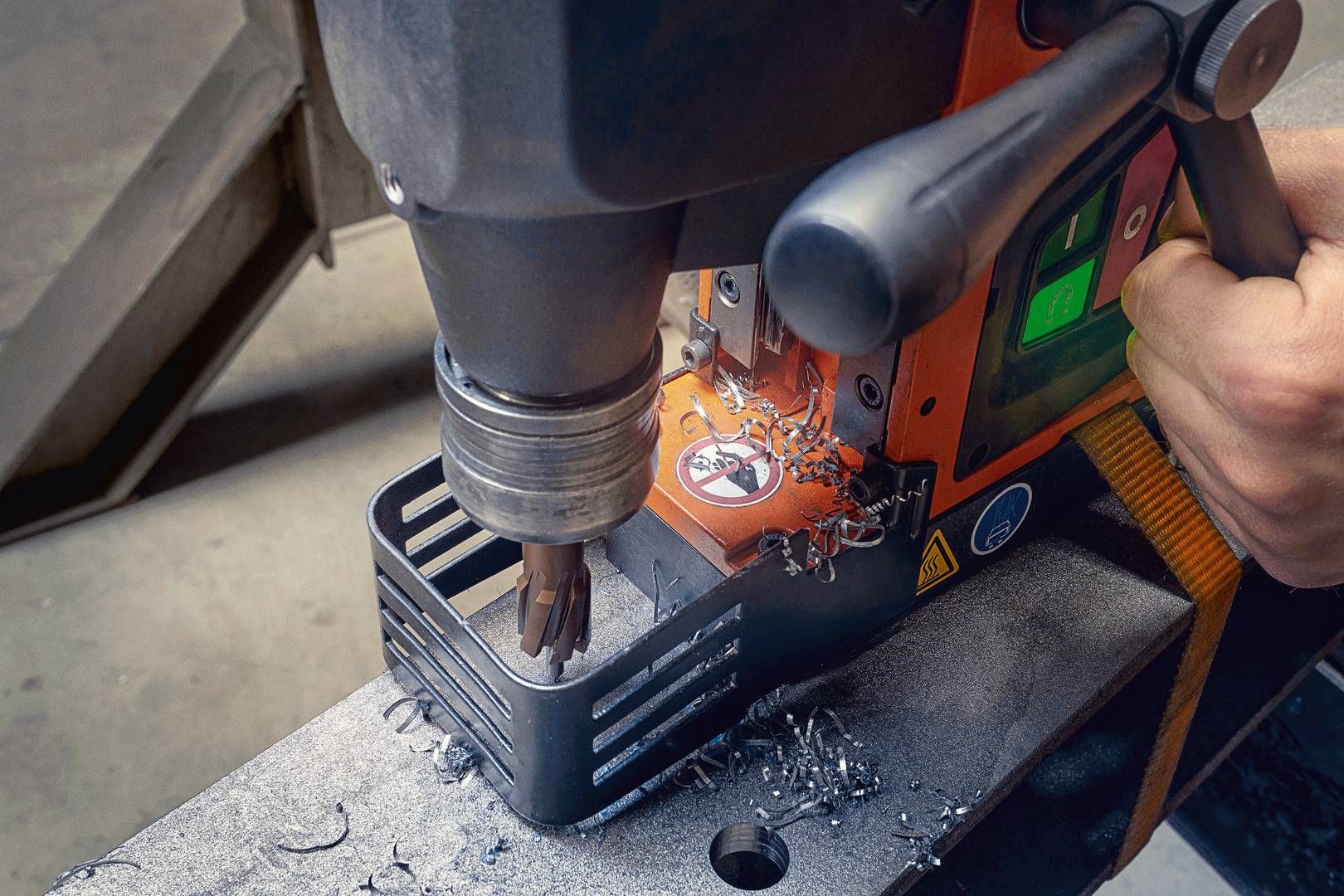 Eine magnetische Bohrmaschine bearbeitet ein Metallstück. Metallspäne sind sichtbar. Sicherheitsaufkleber und Bedienelemente sind zu erkennen.