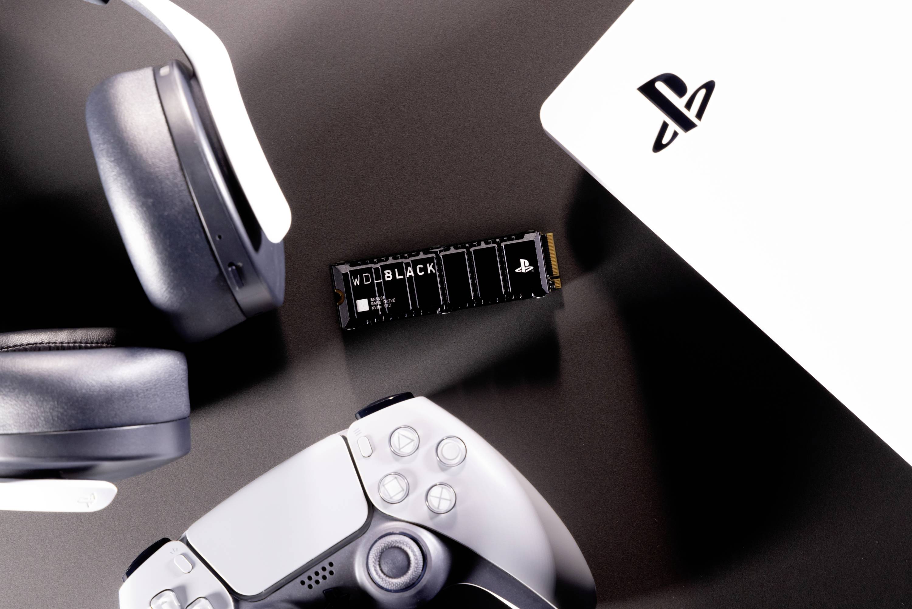 Schwarze Festplatte, weißer Controller und Kopfhörer neben einer Spielekonsole. Thema: Gaming-Zubehör und Technik.