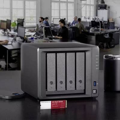 Ein silberner NAS-Server steht auf einem Schreibtisch in einem modernen Büro, umgeben von mehreren Personen an Computern. Im Vordergrund eine WD Red Festplatte.