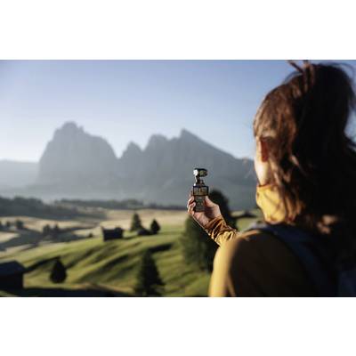 Eine Frau hält eine Kamera und filmt eine Berglandschaft in den frühen Morgenstunden. Im Hintergrund sind Hügel und Berge zu sehen.