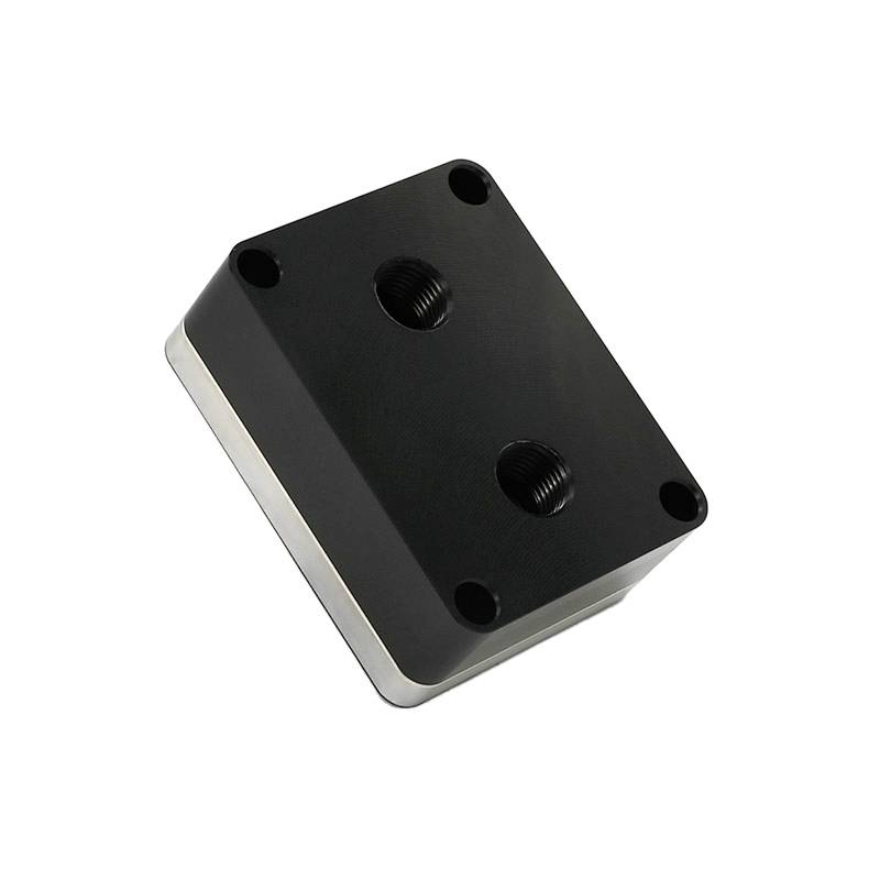 Ein rechteckiger, schwarzer Metallblock mit abgerundeten Ecken und vier Gewindebohrungen, die in einer industriellen Anwendung verwendet werden könnten.