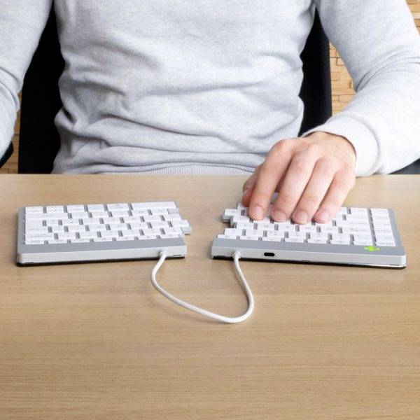 Eine Person tippt auf einer geteilten Tastatur, wobei die Tastaturhälften auf einem Holztisch liegen.