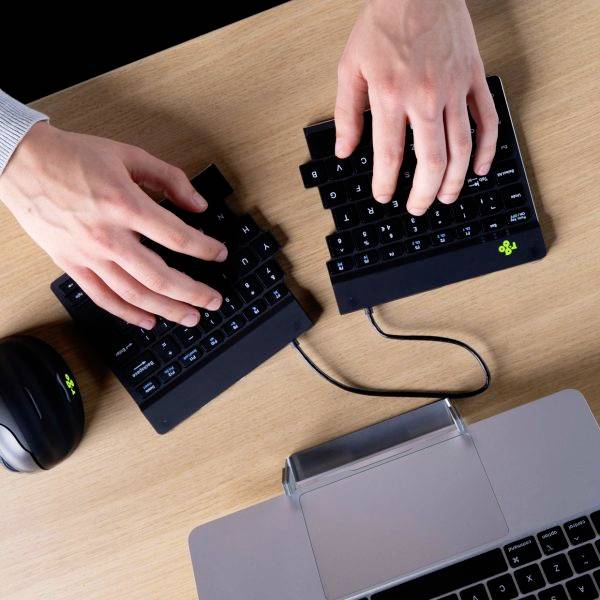Zwei Hände tippen auf einer geteilten ergonomischen Tastatur. Eine Maus befindet sich links.