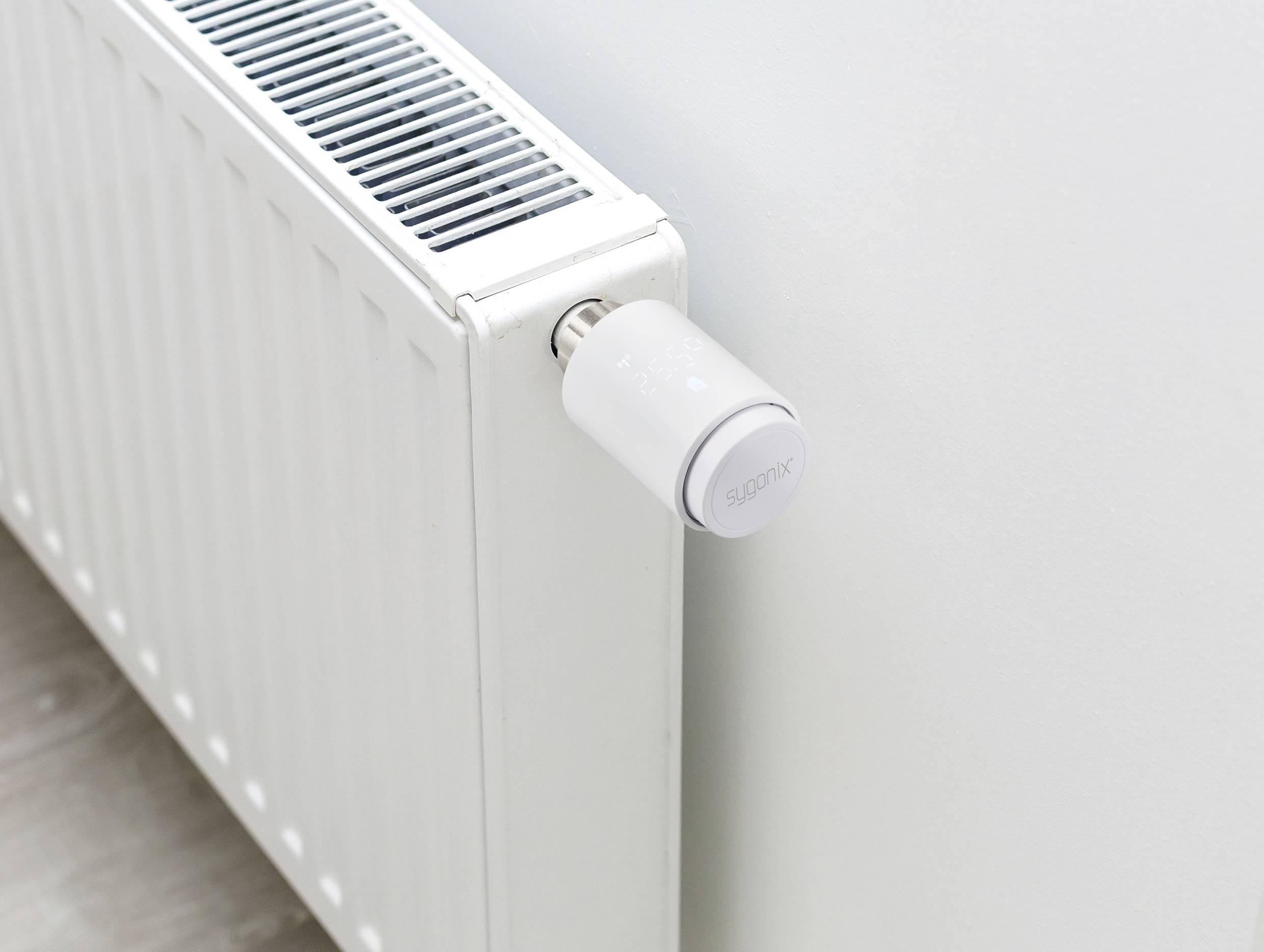Ein weißer Heizkörper mit einem digitalen Thermostat an einer weißen Wand.