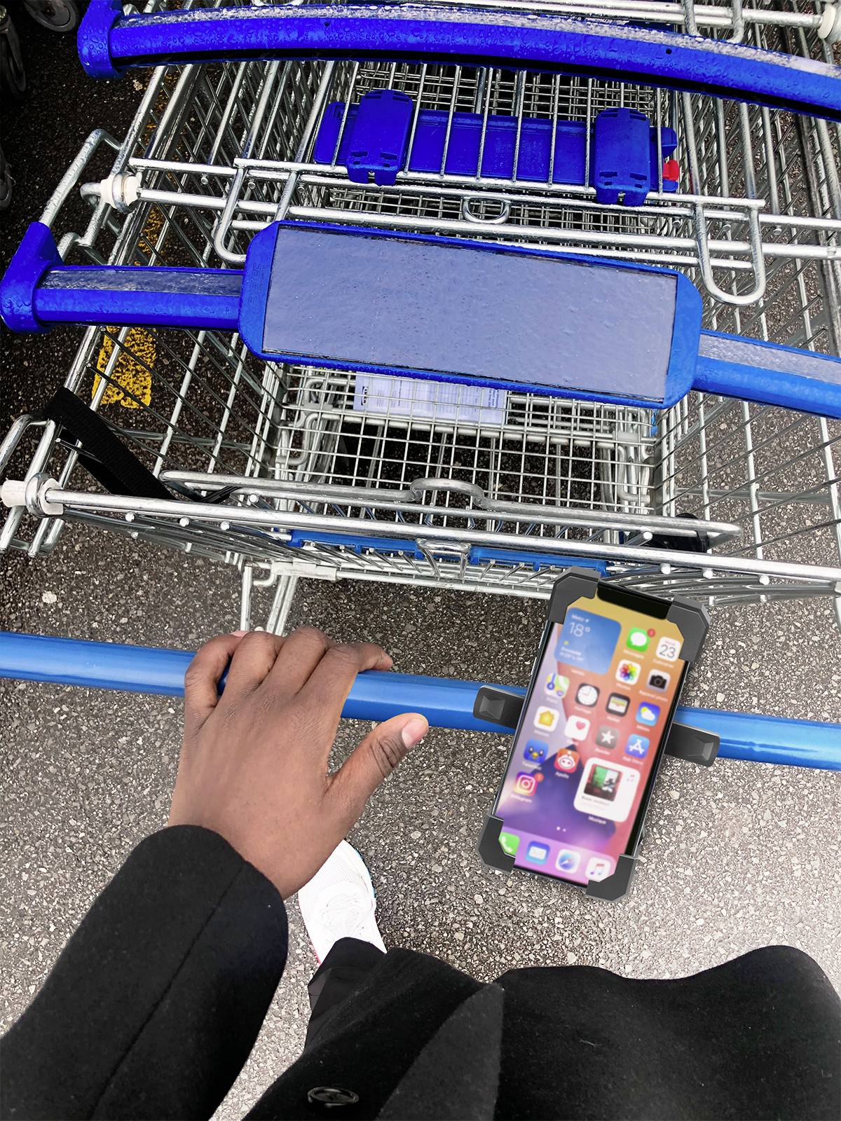 Eine Person hält einen Einkaufswagen im Freien. Ein Smartphone ist am Griff des Wagens befestigt und zeigt eine App-Startseite.