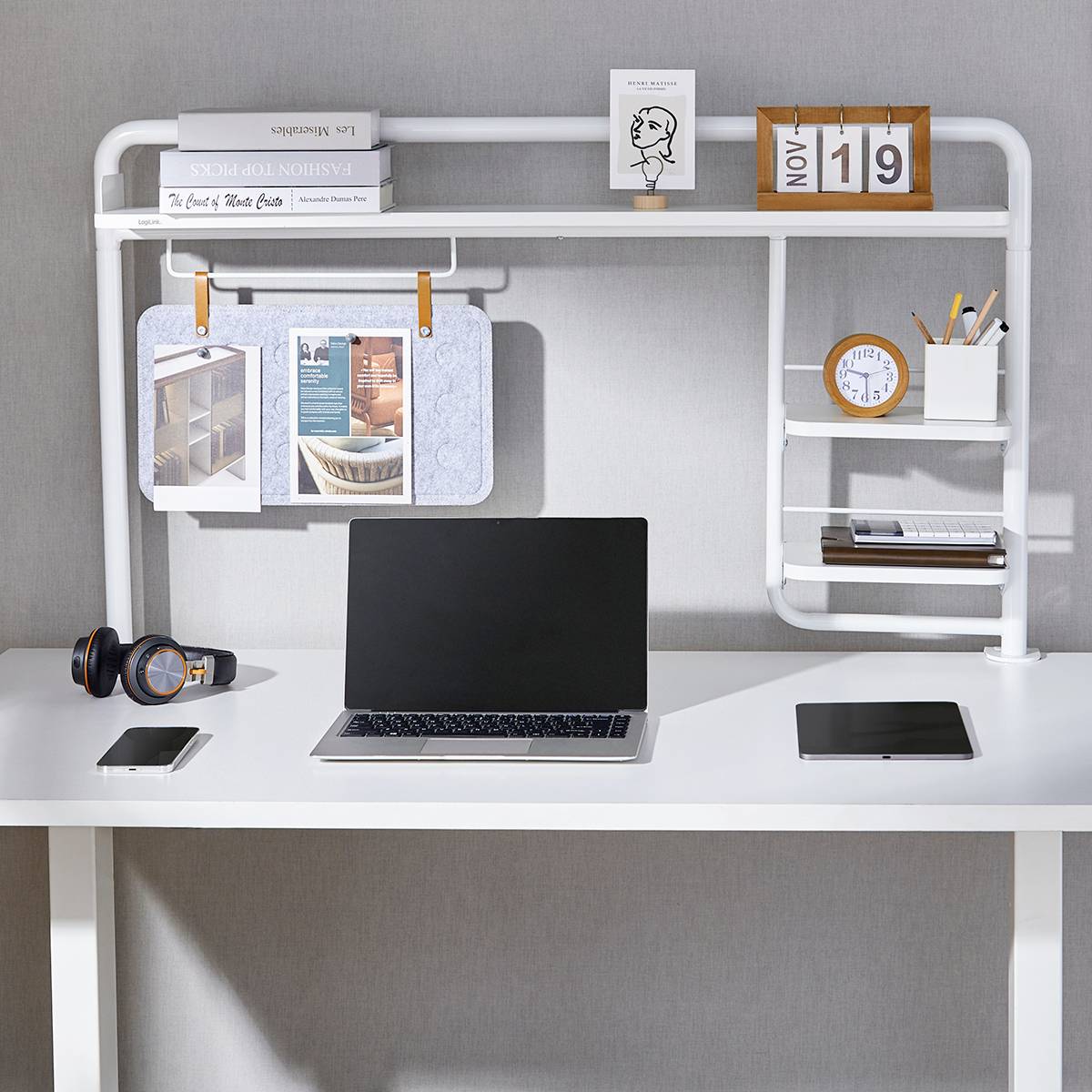 Ein aufgeräumter Schreibtisch mit Laptop, Tablet, Smartphone und Kopfhörern; darüber ein Regal mit Kalender und Notizen.