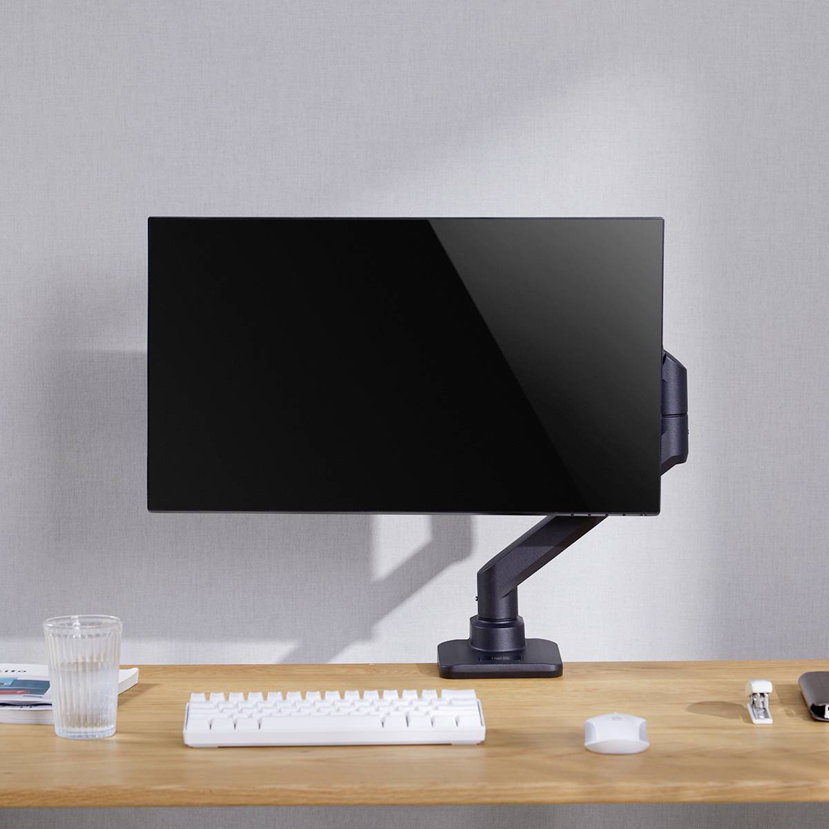 Ein aufgeräumter Schreibtisch mit Monitor auf der linken Seite, Tastatur, Maus, Glas Wasser und Notebooks, sanft beleuchtet.