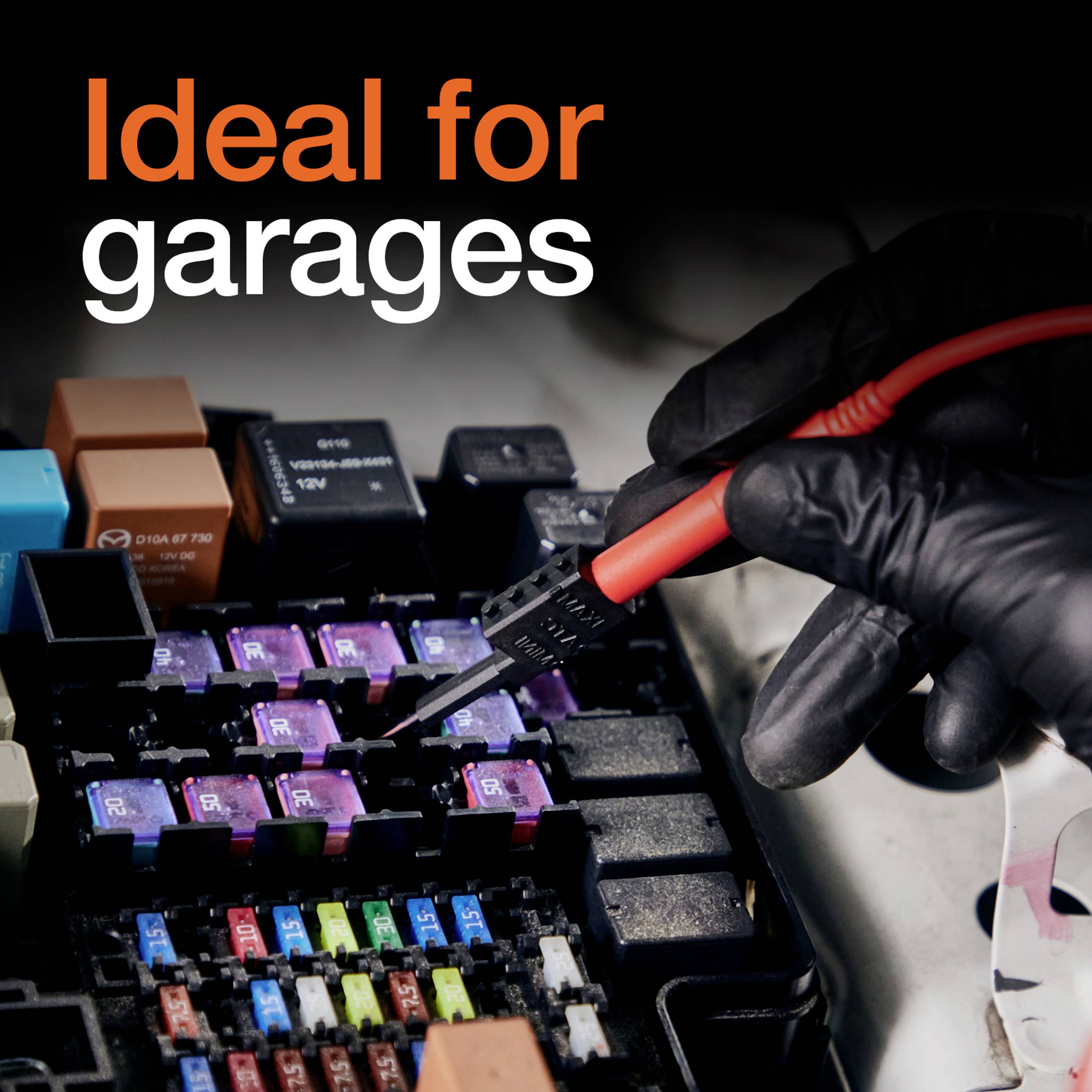 Eine Hand mit rot-schwarzem Handschuh testet mit einem Multimeter verschiedene Autosicherungen in einer Sicherungsdose.