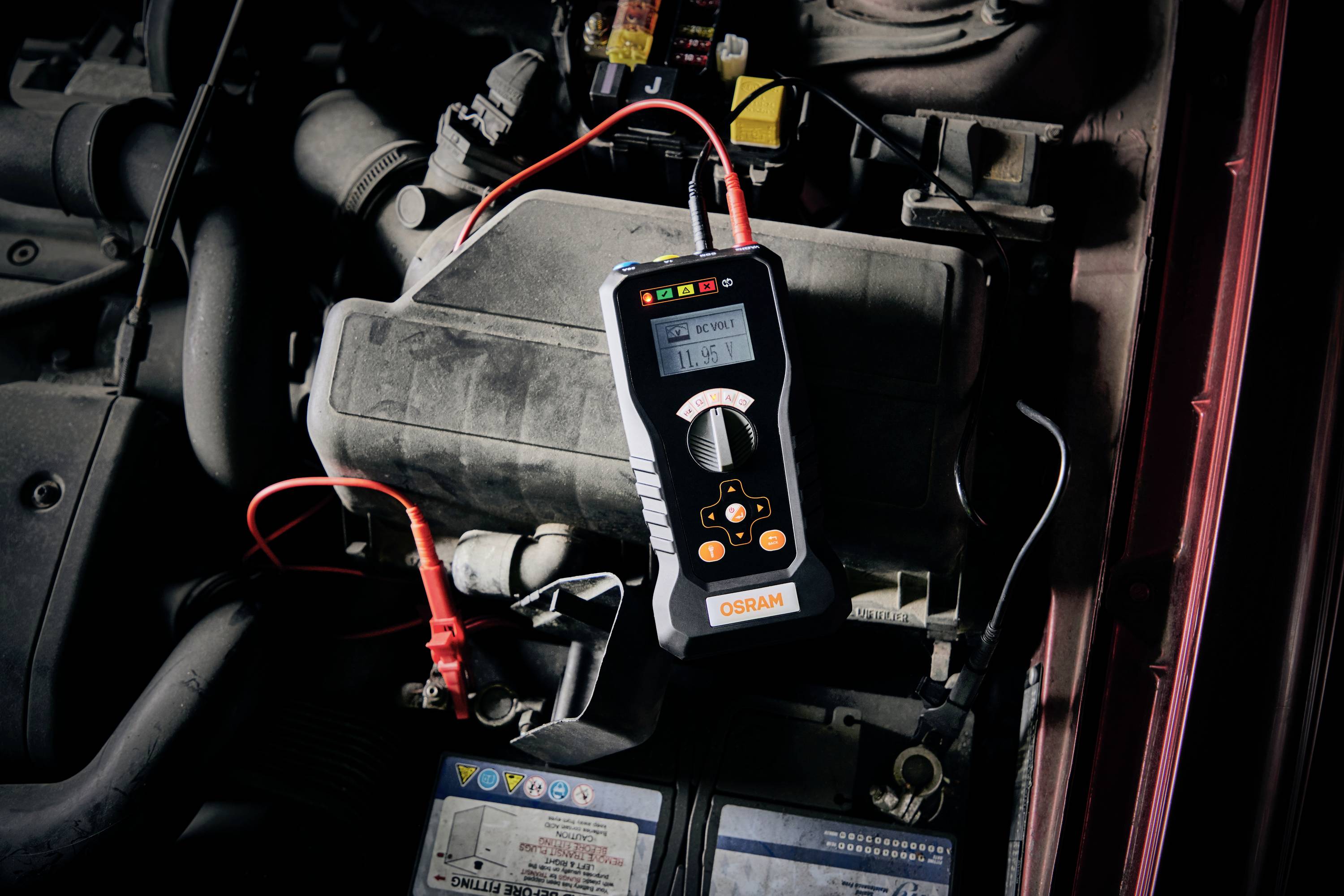 Ein Diagnosegerät sitzt auf einer Autobatterie, zeigt eine Messung auf dem Display an. Batteriekabel sind angeschlossen.