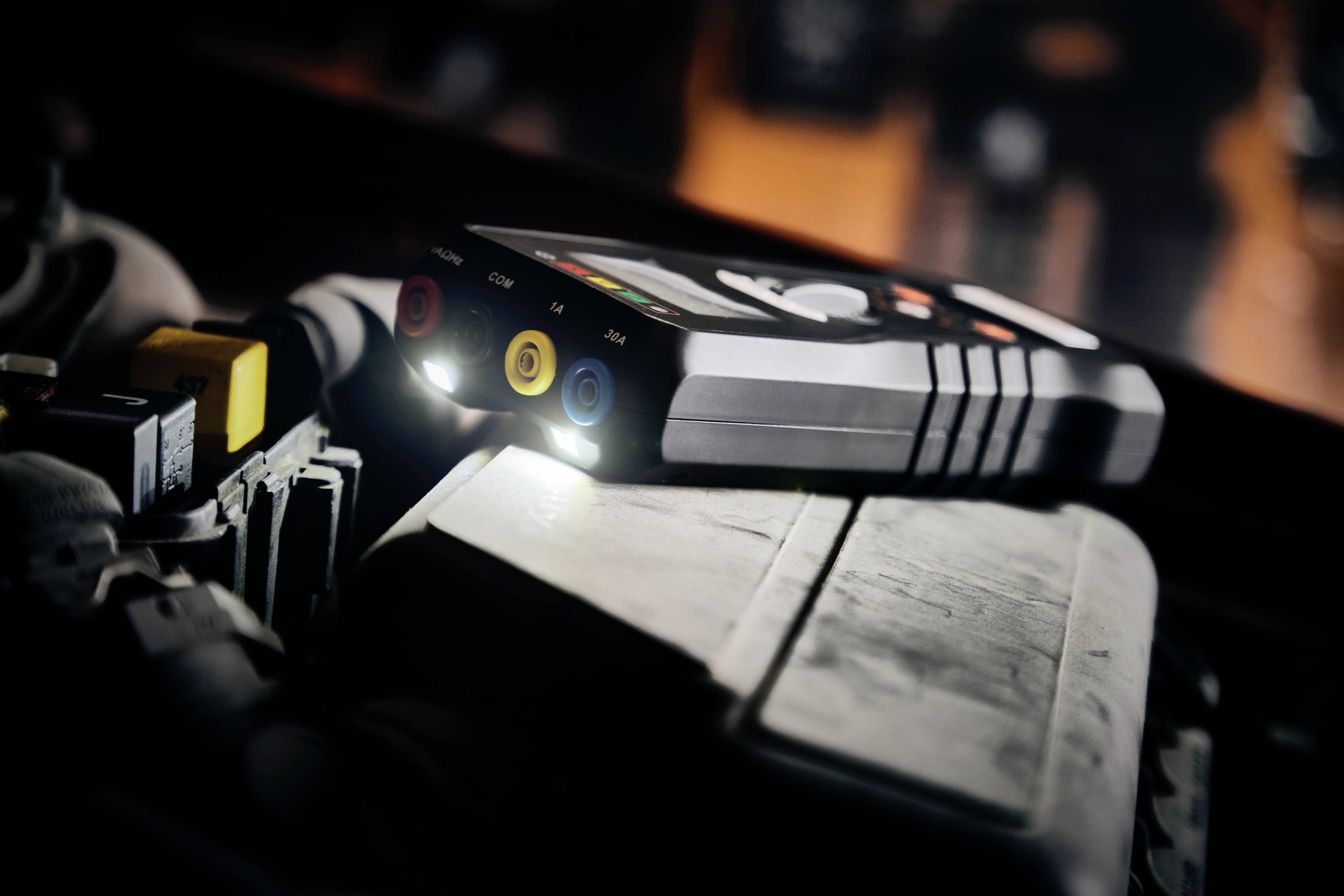 Multimetergerät mit leuchtenden Anzeigen auf einem Motorblock, zeigt gelbe, rote und blaue Anschlussbuchsen, beleuchtet den Arbeitsbereich.