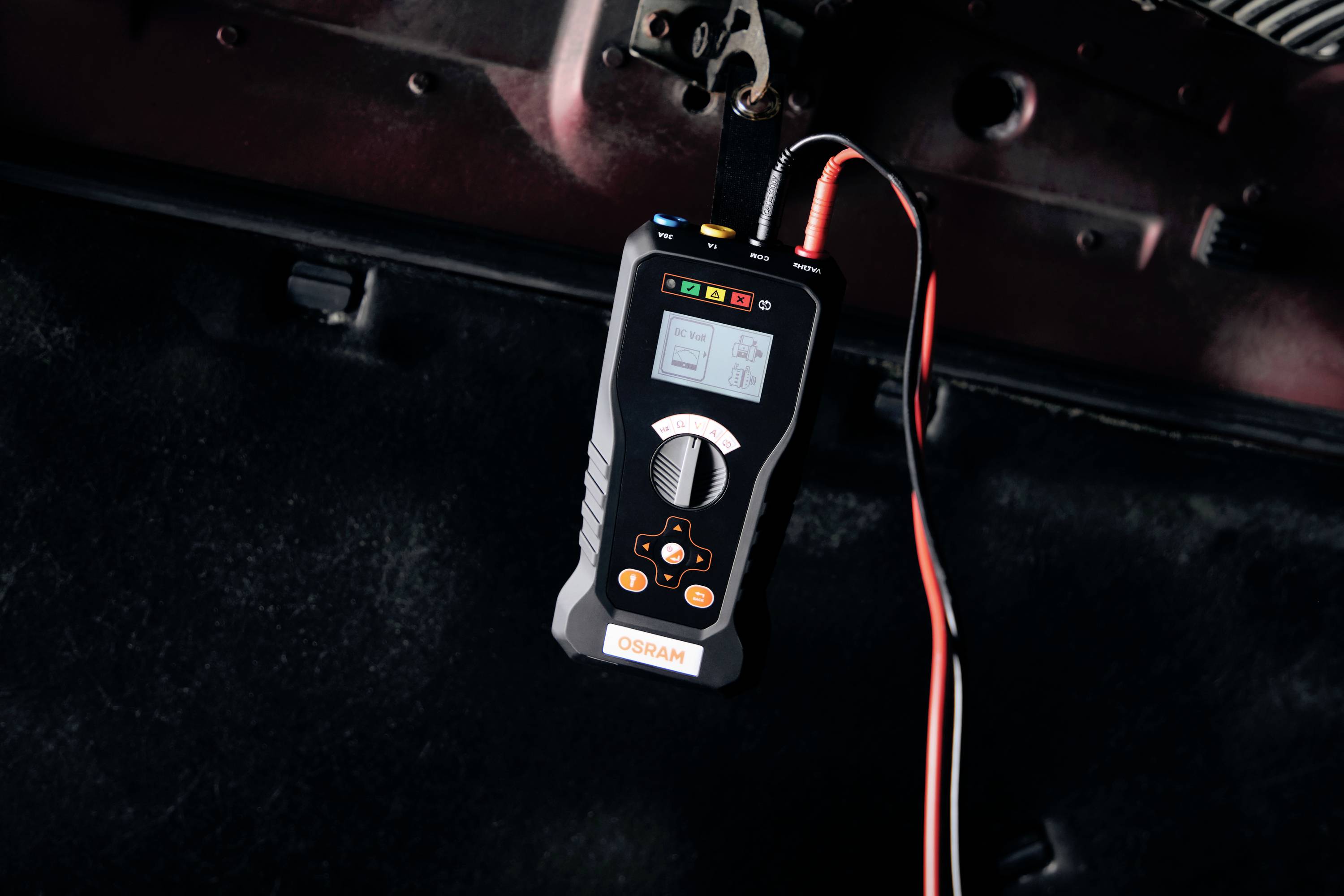 Ein elektrisches Prüfgerät hängt an Kabeln, zeigt Messwerte auf einem Display an, verwendet zur Fahrzeugdiagnose.