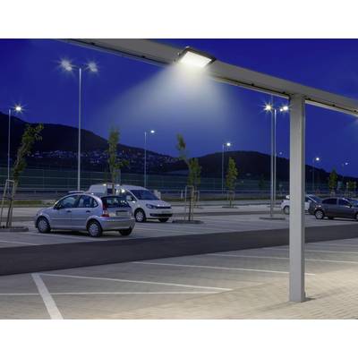 Beleuchteter Parkplatz bei Nacht mit mehreren geparkten Autos und im Hintergrund eine hügelige Landschaft mit Lichtern.