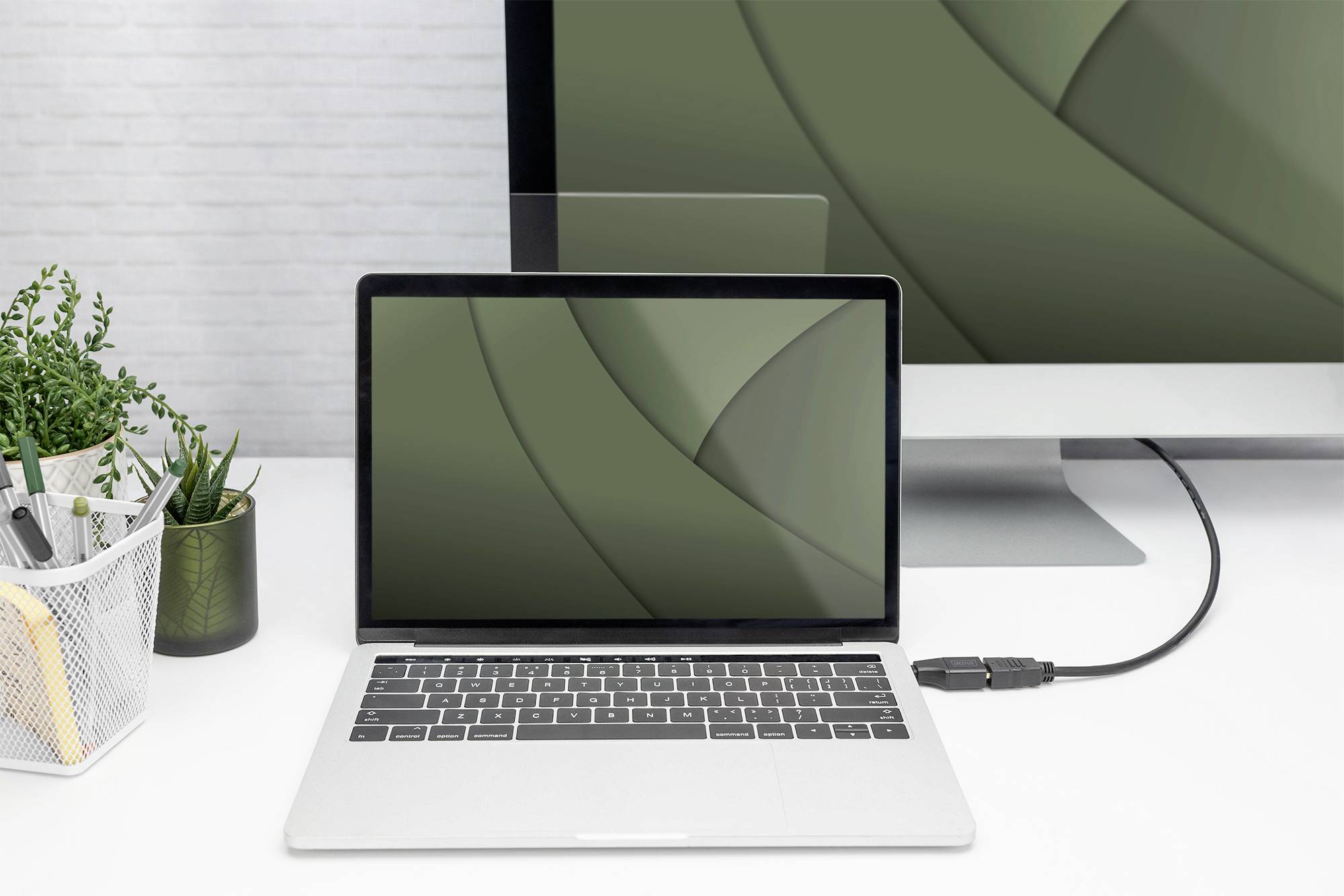 Ein Laptop ist mit einem Desktop-Computer verbunden. Beide Bildschirme zeigen dasselbe grüne Hintergrundmuster.