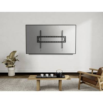 Ein Wohnzimmer mit einer hellen Wand. Ein TV-Wandhalter ohne Fernseher ist montiert. Darunter steht ein Holztisch mit Teeservice.