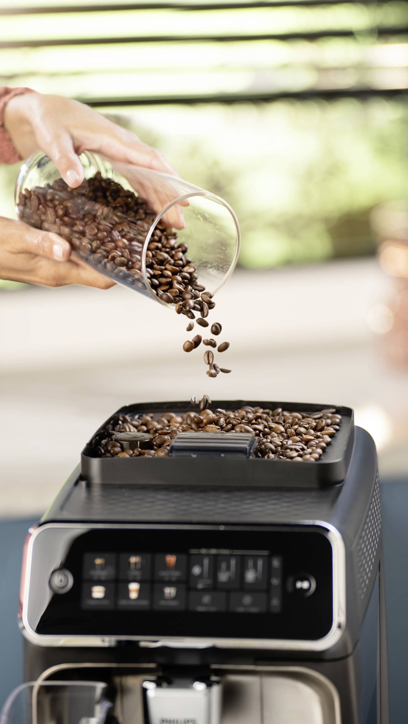 Eine Person füllt Kaffeebohnen in einen Vollautomaten. Die Maschine zeigt ein Bedienfeld mit mehreren Knöpfen.