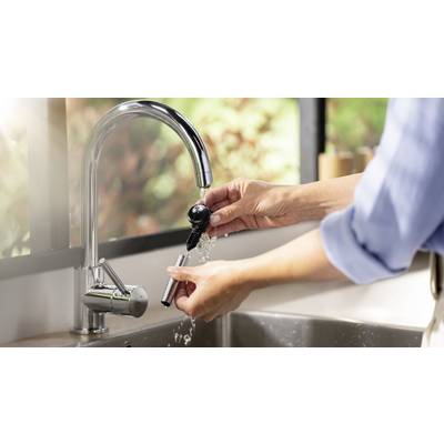 Jemand spült einen elektrischen Rasierkopf unter einem Wasserhahn in einer modernen Küche ab.