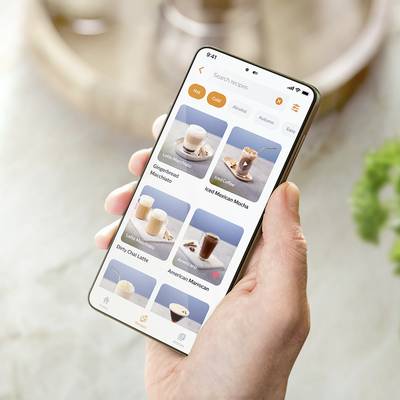 Eine Hand hält ein Smartphone, das eine Getränkeauswahl in einer App zeigt, darunter Café Latte, Kaffee und Milchshakes.