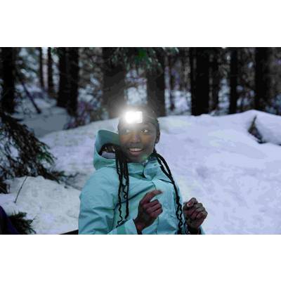 Person im Wintermantel mit Stirnlampe im verschneiten Wald, lächelnd und nach links blickend.