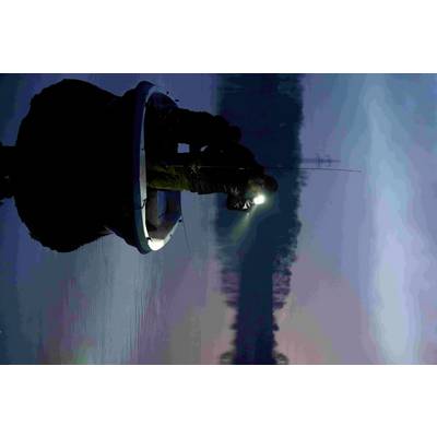 Zwei Personen angeln nachts auf einem kleinen Boot auf einem ruhigen See. Eine Person hält eine Taschenlampe, die das Wasser beleuchtet.
