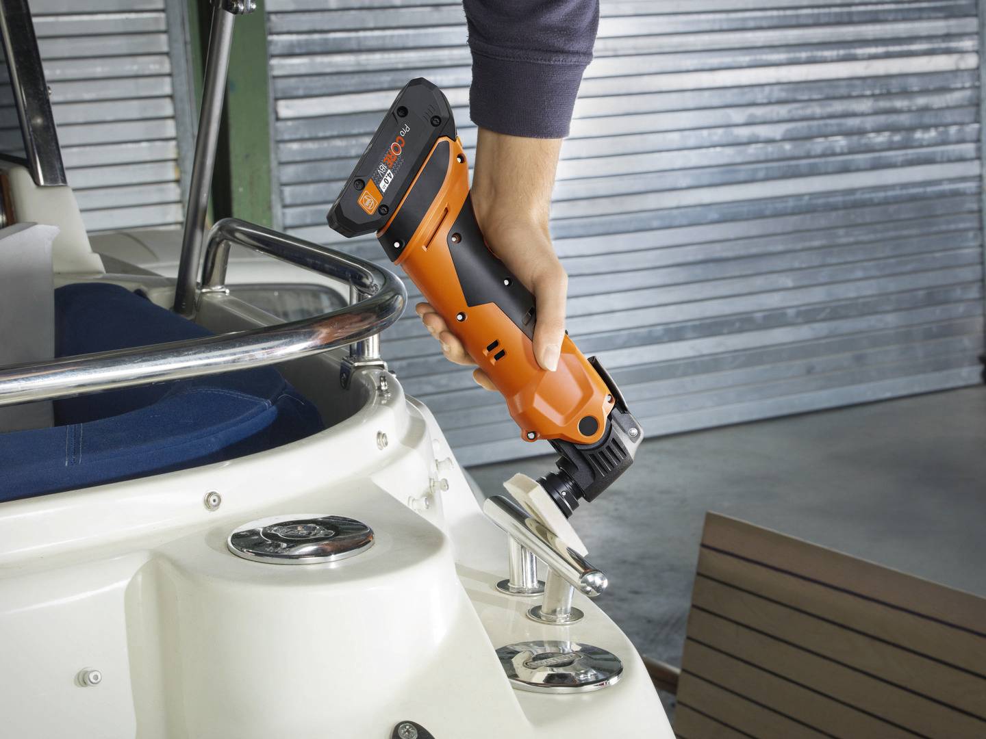 'Eine Person hält ein orangenes Elektrowerkzeug über einem Griff an einem Boot. Der Hintergrund zeigt eine Garagenumgebung.'