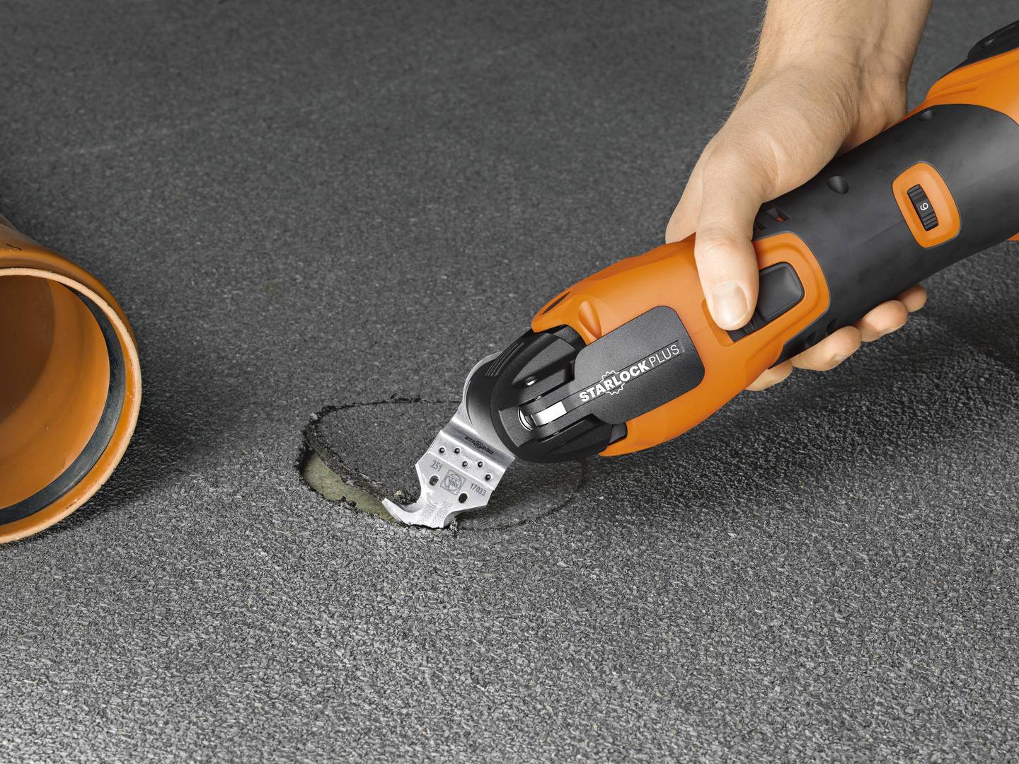 Eine Person schneidet mit einem oszillierenden Multifunktionswerkzeug in einen Betonboden neben einem orangefarbenen Rohr.