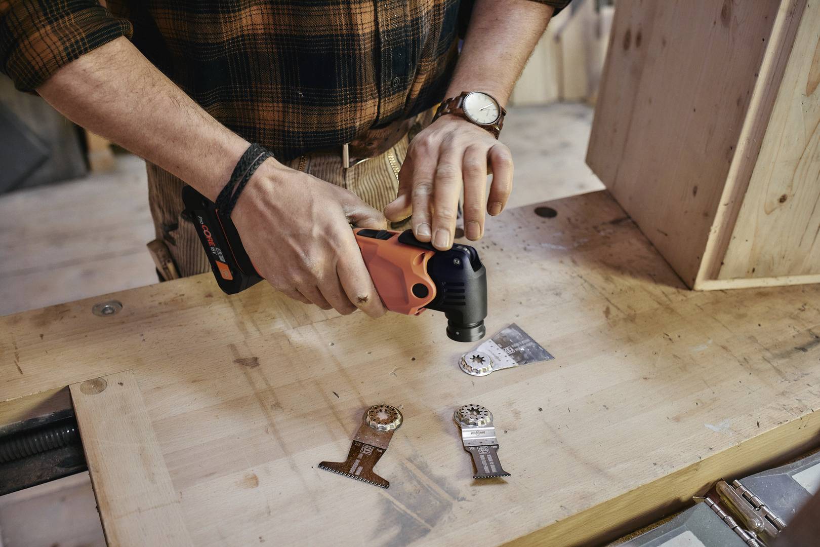 Eine Person benutzt ein oszillierendes Multifunktionswerkzeug auf einem Holztisch, um eine Metallplatte zu bearbeiten.