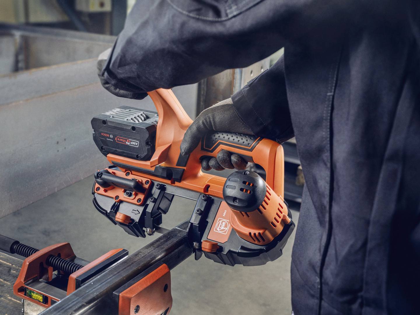 Eine Person in Arbeitskleidung bedient ein oranges Elektrowerkzeug, um Metall in einer Werkstatt zu bearbeiten.