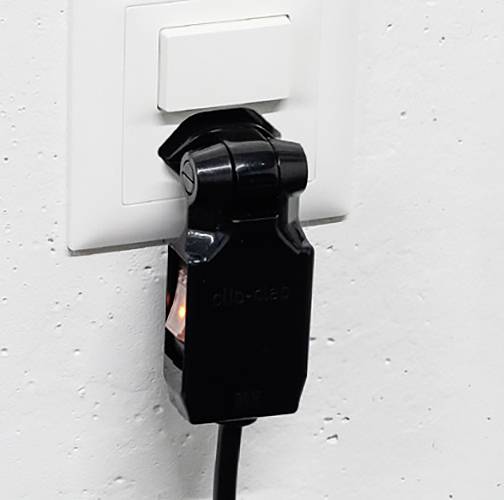 Eine schwarze Schaltervorrichtung ist an eine weiße Steckdose an der Wand angeschlossen. Ein Kabel ragt aus dem Gerät heraus.