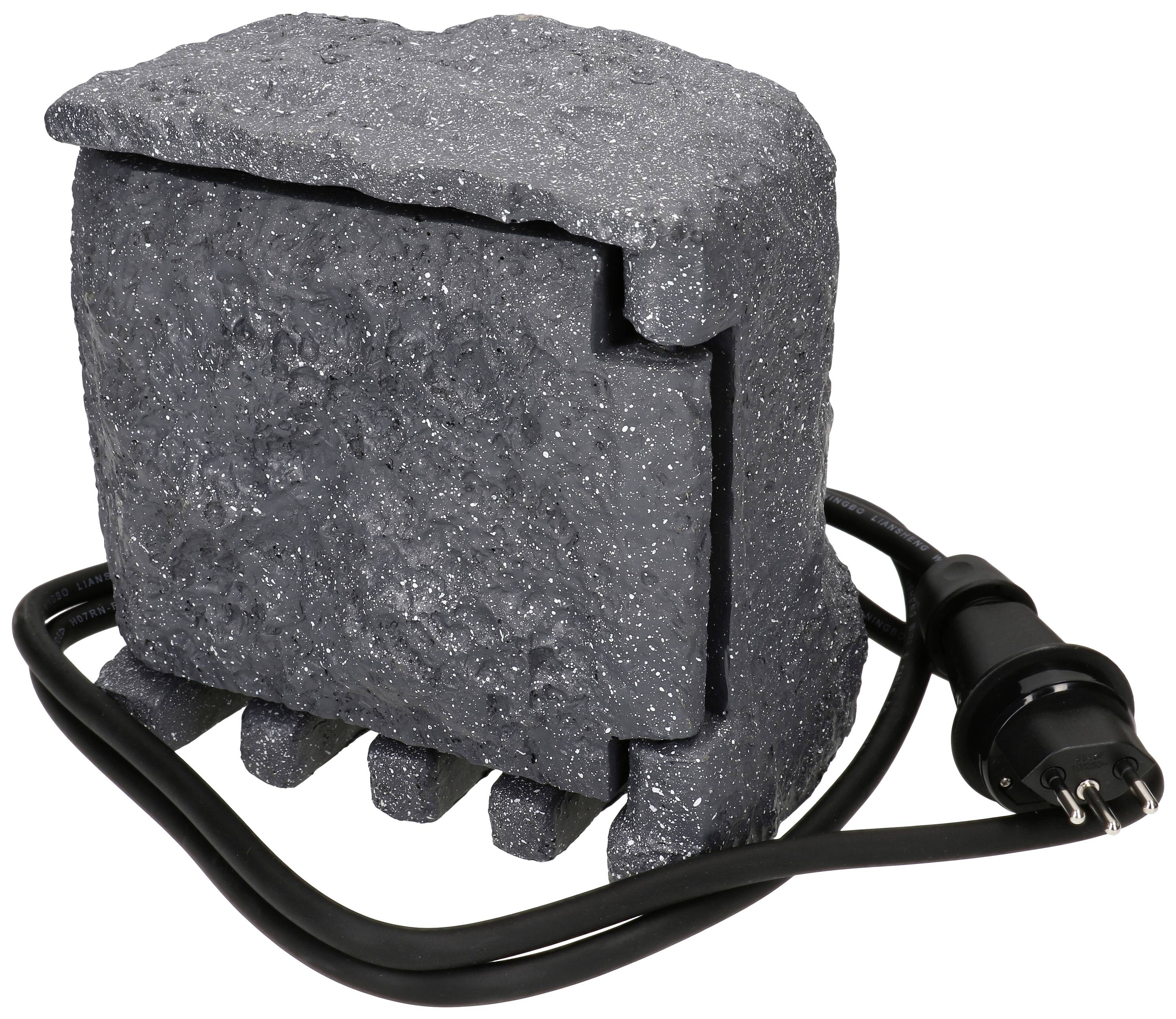 Ein schwarzer, steinähnlicher Block mit einem sichtbaren Stromkabel und Stecker liegt davor.