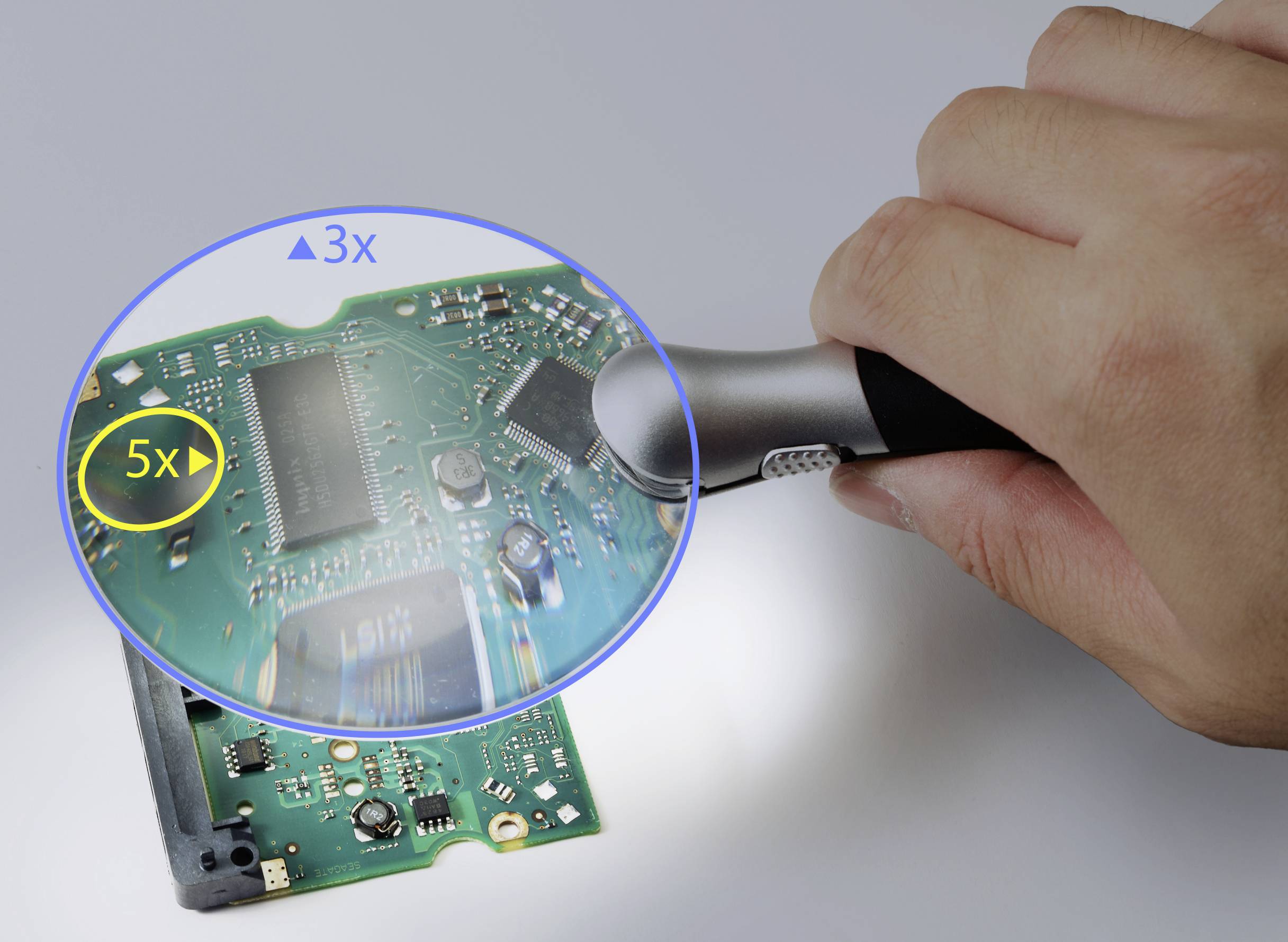 'Hand hält Lupe über elektronische Schaltung, vergrößert Details zur leichteren Betrachtung kleinster Komponenten.'