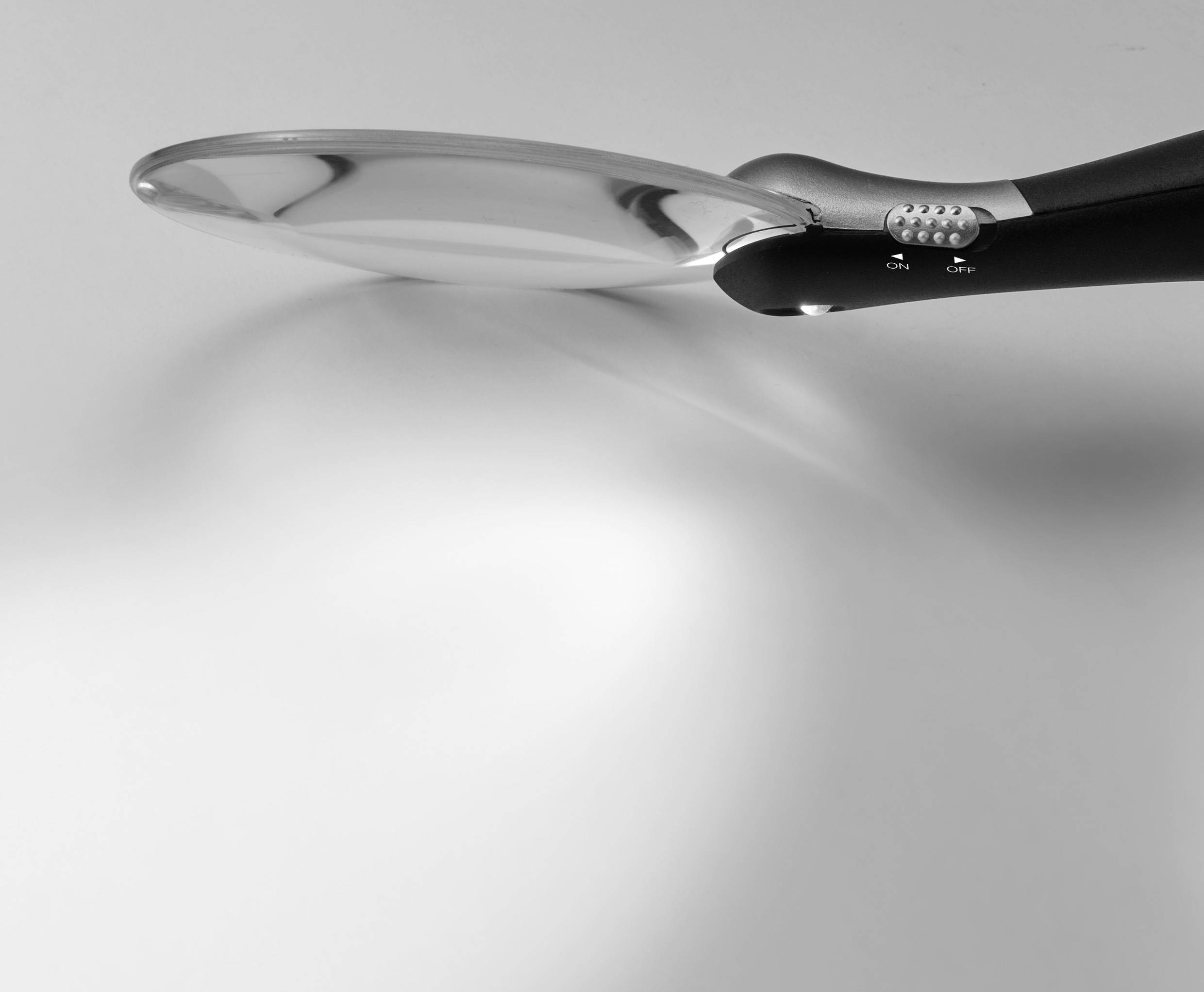 Ein silberner Löffel liegt diagonal auf einer weißen Oberfläche. Der Griff ist schwarz und leicht gebogen. Der Hintergrund ist schlicht.