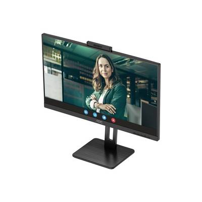 Ein Monitor zeigt eine Frau in einem grünen Blazer in einem Videoanruf. Sie steht mit verschränkten Armen in einem Büro.