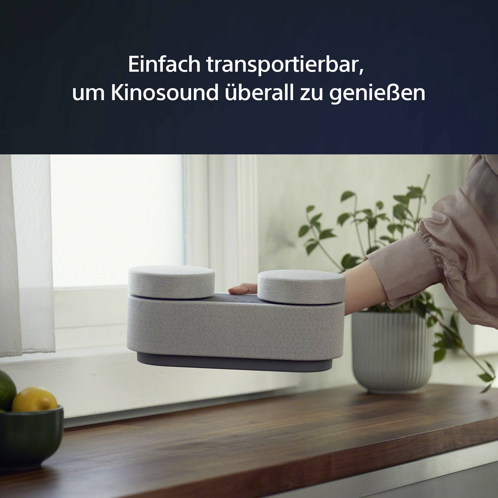 Ein tragbarer Lautsprecher wird auf einem Tisch in einer Wohnung gezeigt. Der Text sagt: 'Einfach transportierbar, um Kinosound überall zu genießen'.