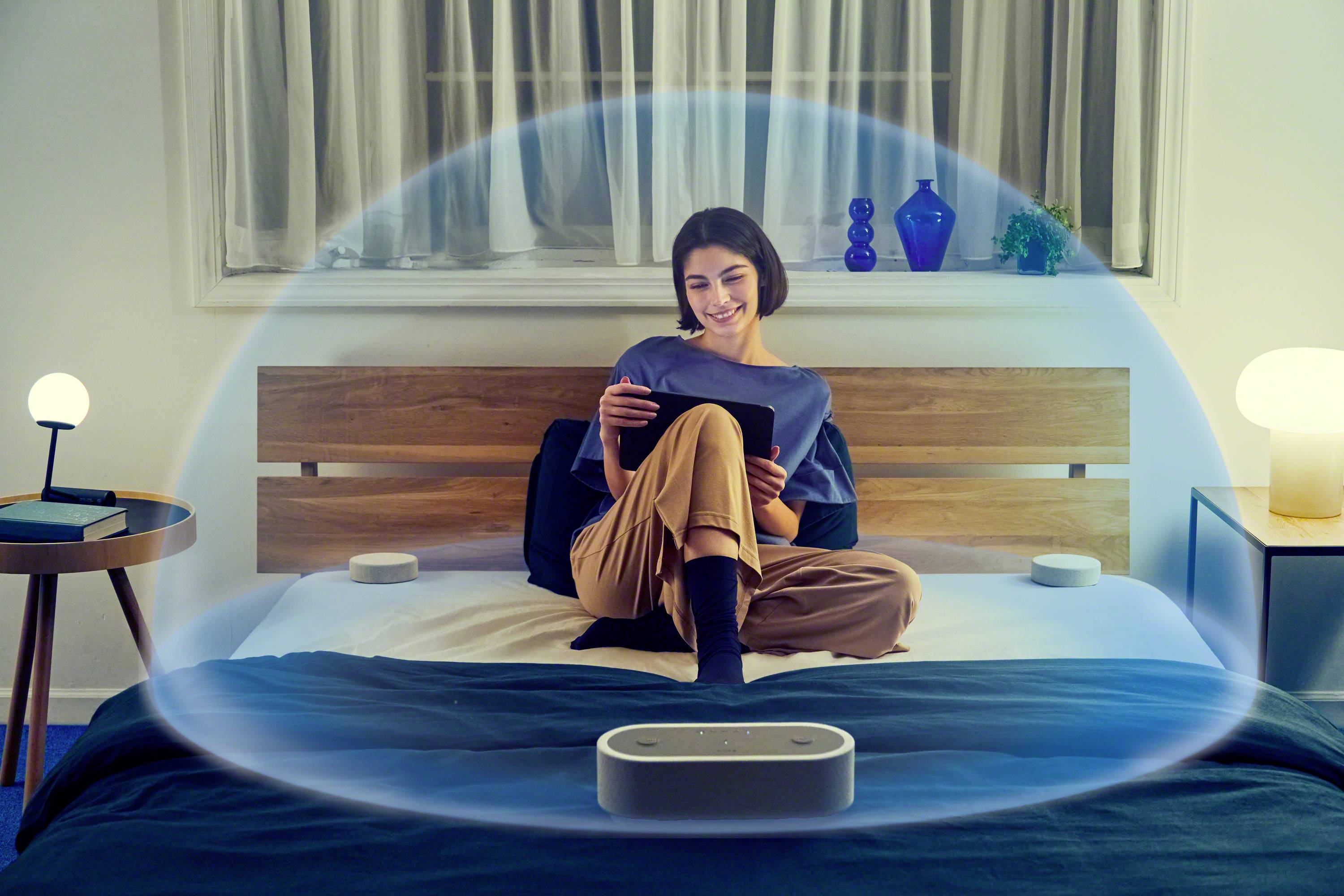 Frau sitzt auf dem Bett, umgeben von transparentem blauen Bogen, liest auf Tablet. Technologie für Privatsphäre oder Meditation.