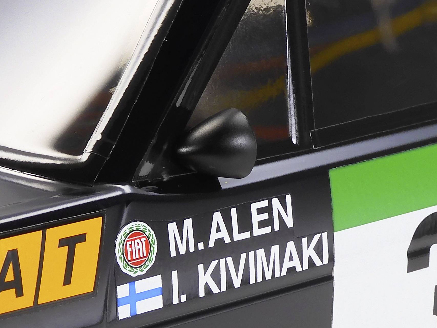 Nahaufnahme eines Rallyeautos mit Namen 'M. Alen' und 'I. Kivimaki' auf der Tür, neben einem Fiat-Logo. Finnische Flagge ist sichtbar.