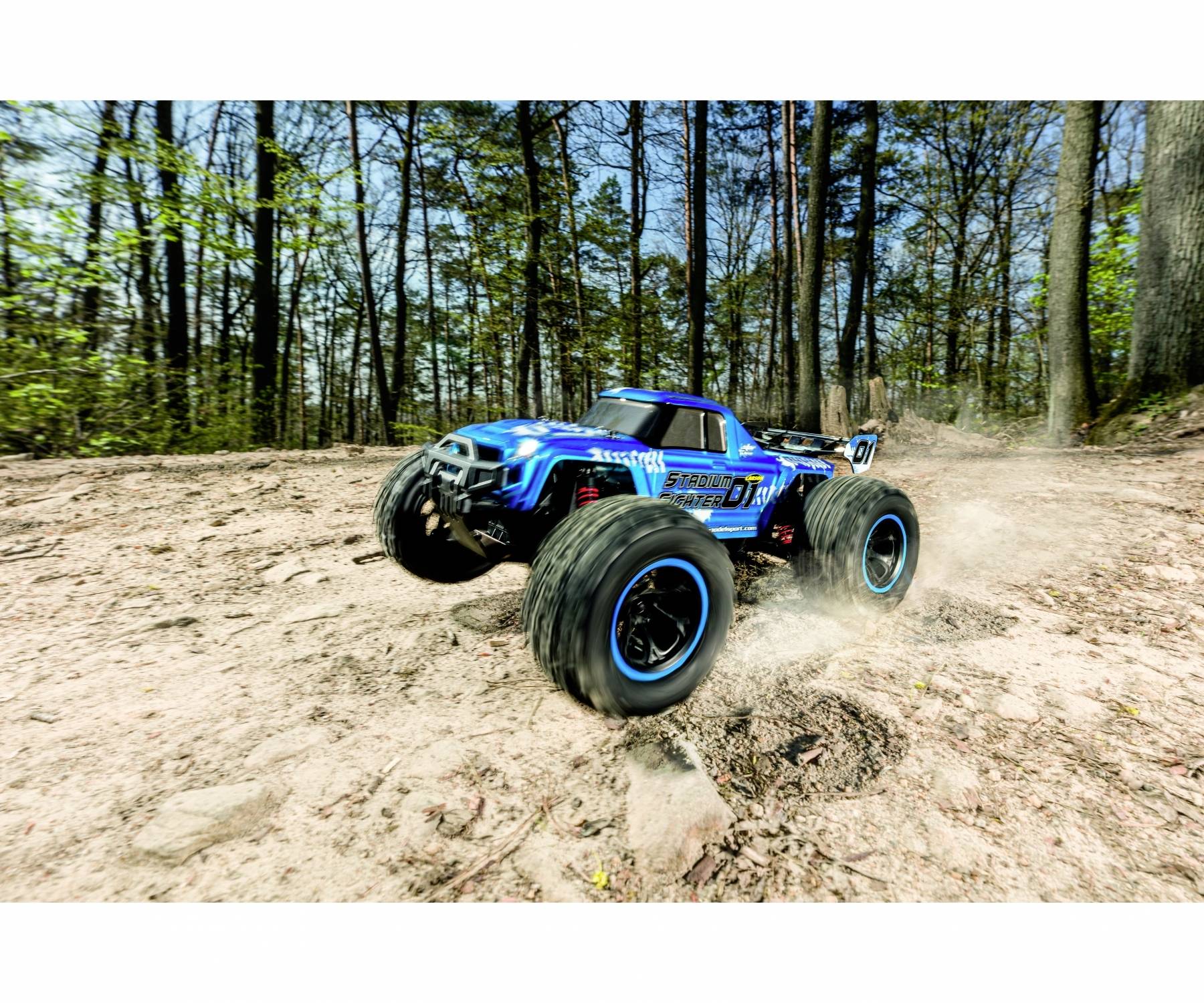 Ein blauer, ferngesteuerter Geländewagen fährt mit hoher Geschwindigkeit über eine staubige, felsige Waldfläche.