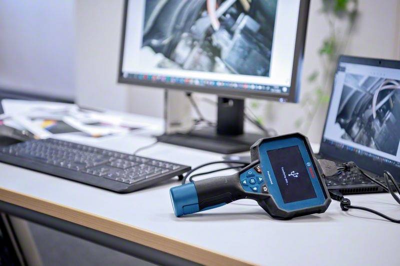 Ein Tisch mit einem Computer und einem Handgerät, vermutlich ein Diagnosewerkzeug. Auf dem Monitor ist ein unscharfes Bild zu sehen.