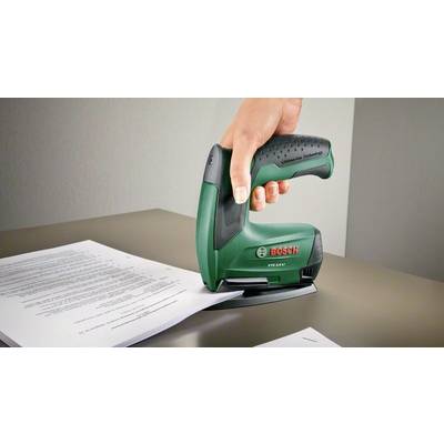 Eine Hand hält einen grünen Bosch Elektrotacker und tackert Papier auf einem Tisch fest.