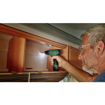 Ein Mann bohrt mit einem Elektrowerkzeug in einen Holzschrank im Wohnmobil, trägt Schutzbrille, konzentriert auf die Arbeit.