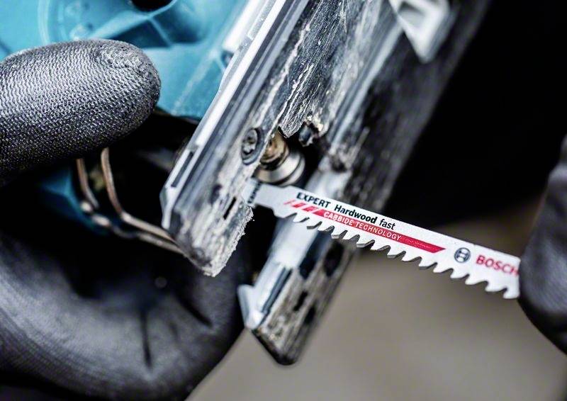 Eine Hand hält sägeblatt aus der Nähe, das in eine elektrische Stichsäge eingesetzt wird. Das Blatt ist für Hartholz geeignet.