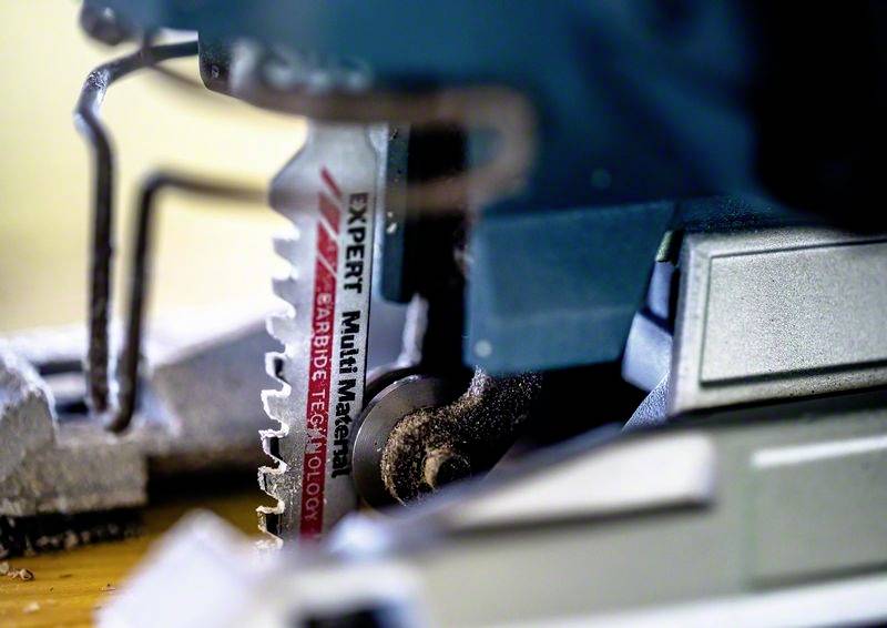Nahaufnahme einer Stichsäge mit eingesetztem Sägeblatt. Fokus liegt auf dem Blatt mit der Aufschrift 'Expert Multi Material, Carbide Technology'.