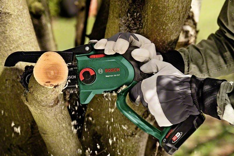 Eine Person schneidet einen Ast mit einer elektrischen Kettensäge von Bosch. Nahaufnahme zeigt die Präzision und Kontrolle beim Schneiden.