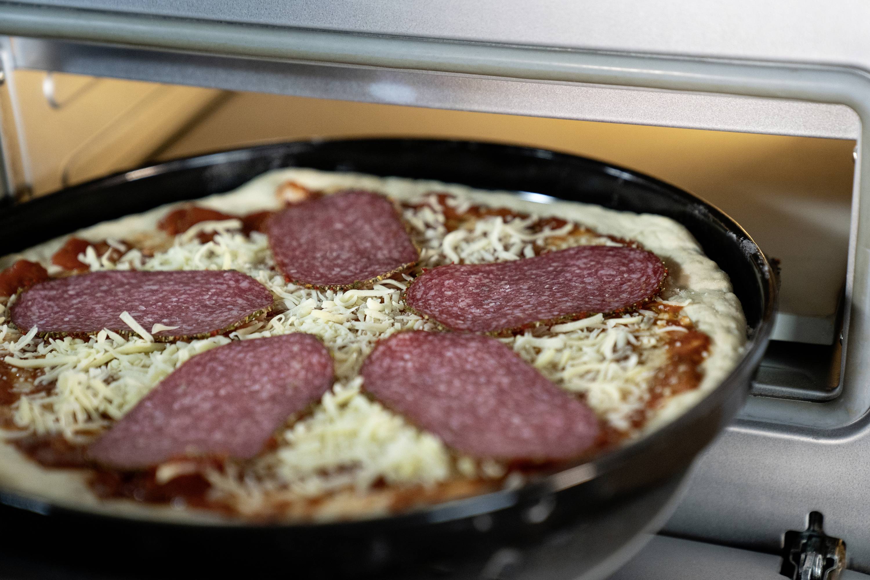 Pizza im Ofen mit Käseschicht und fünf großen Salami-Scheiben, die über den Teig verteilt liegen, während sie gebacken wird.