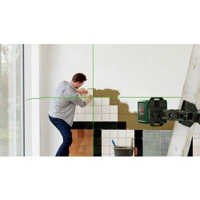 Ein Mann bringt Fliesen an einer Wand an. Eine Laserhilfe projiziert grüne Linien zur korrekten Ausrichtung. Eine Leiter steht neben ihm.