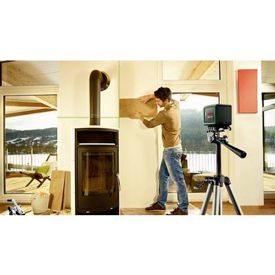Ein Mann installiert neben einem Ofen eine Holzplatte an der Wand. Ein Laser-Nivelliergerät ist auf einem Stativ ausgerichtet.