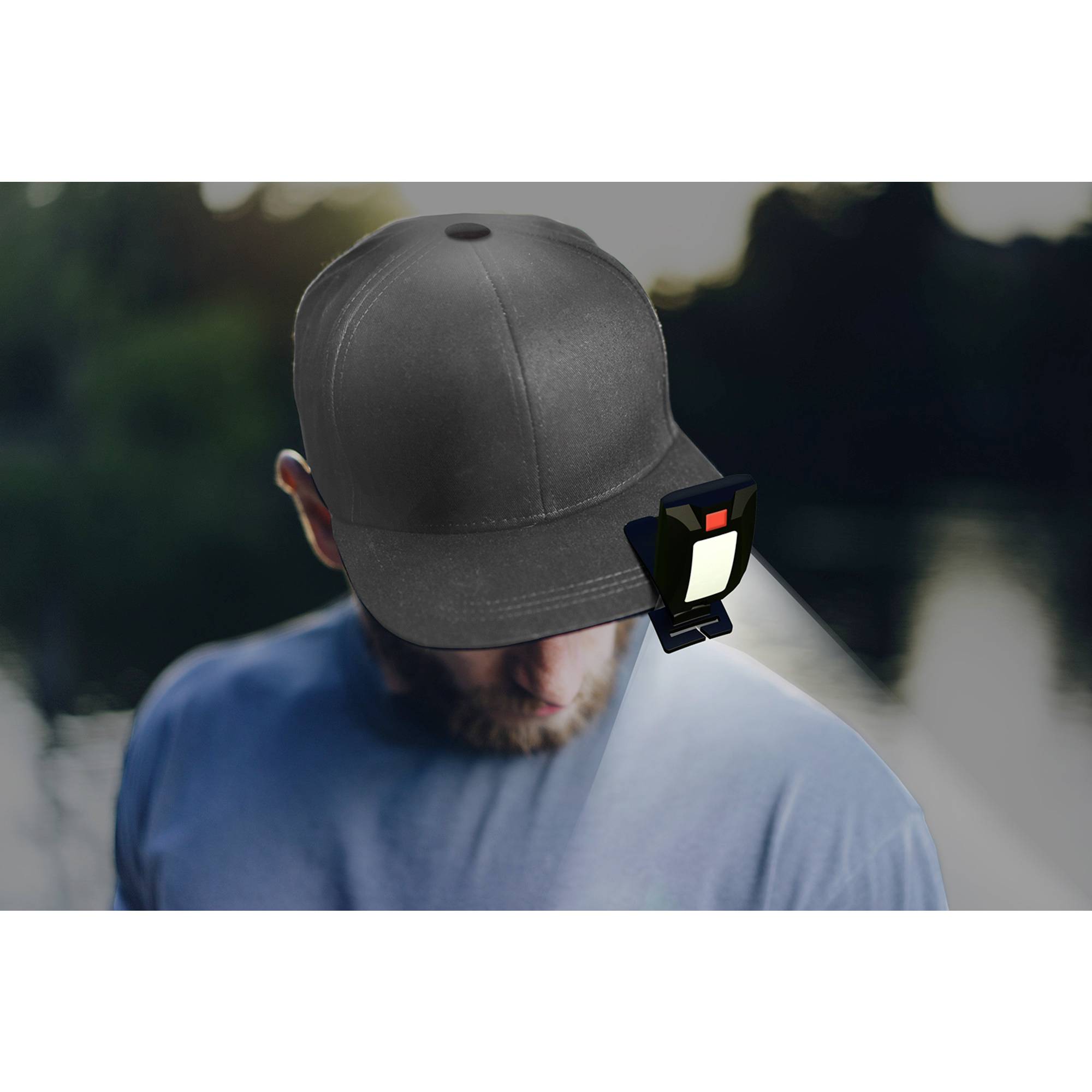 Eine Person trägt eine schwarze Baseballkappe im Freien, mit einer kleinen rechteckigen Lampe vorne befestigt, die nach unten leuchtet.