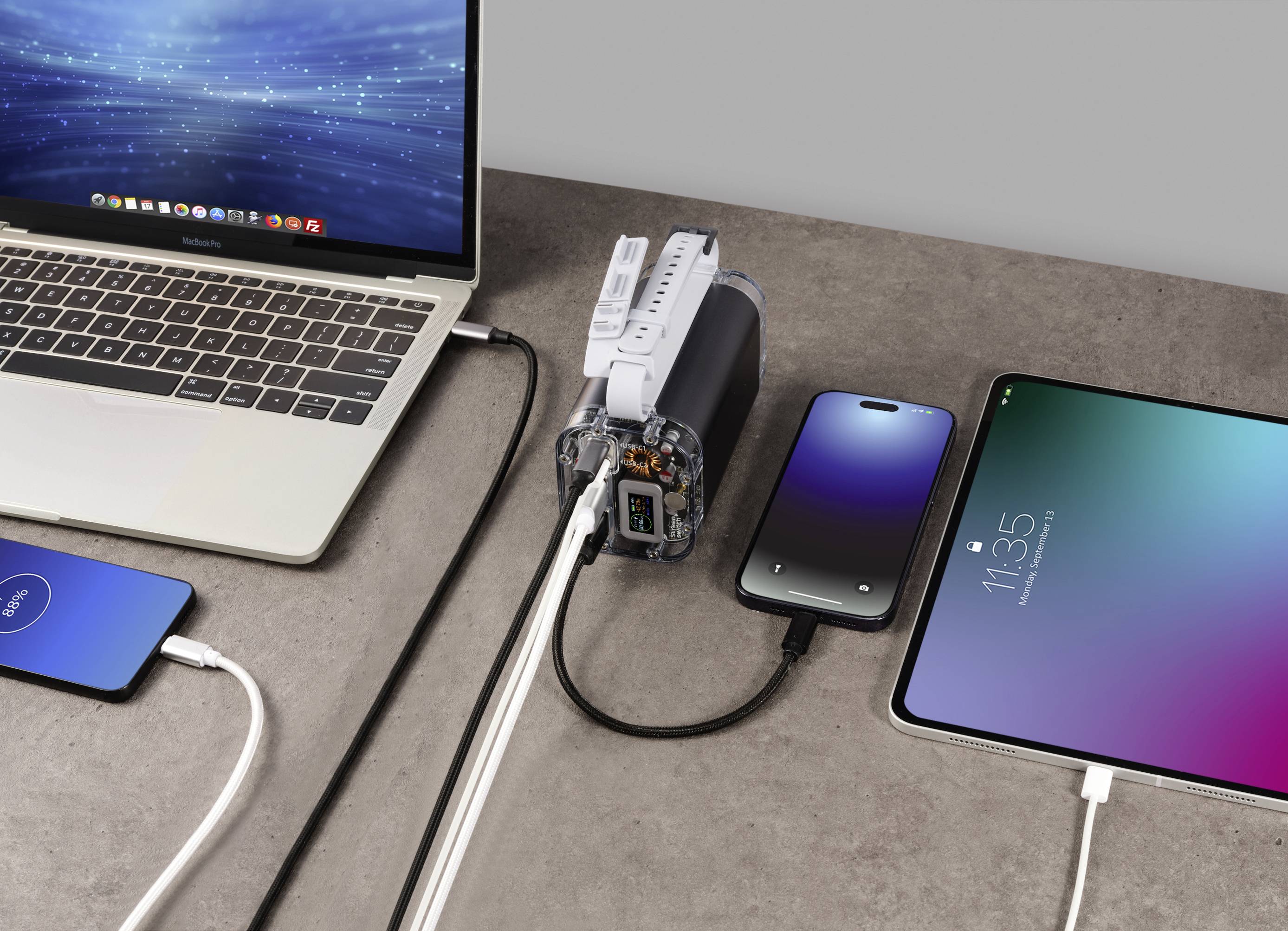 Laptop, Smartphone, Tablet und Ladegerät auf einem Tisch. Alle Geräte sind miteinander verbunden, was die Vielseitigkeit der Anschlüsse zeigt.