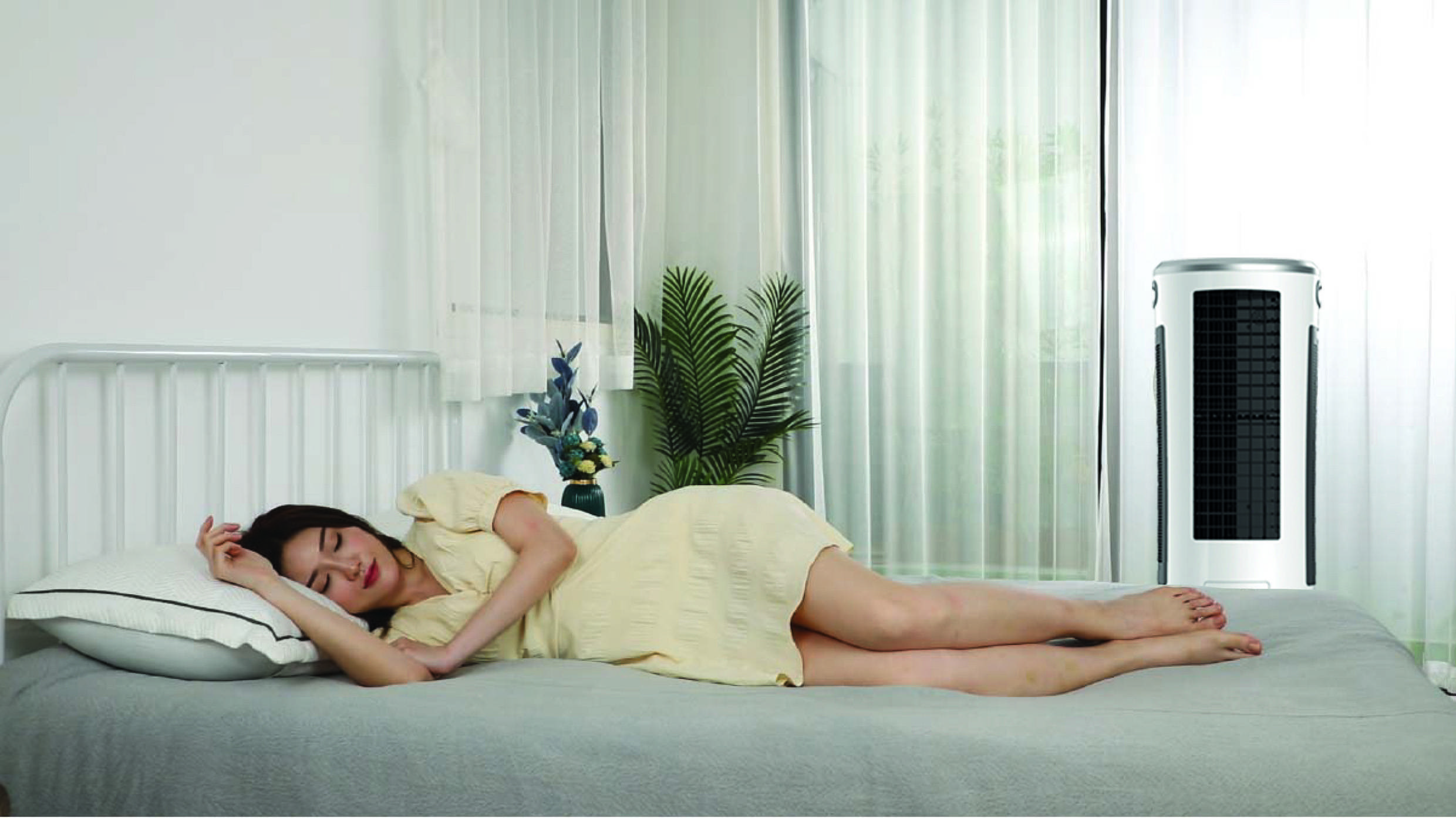 Eine Frau liegt auf einem Bett und schläft; rechts im Raum steht ein Luftkühler, umgeben von Pflanzen und hellem Licht.