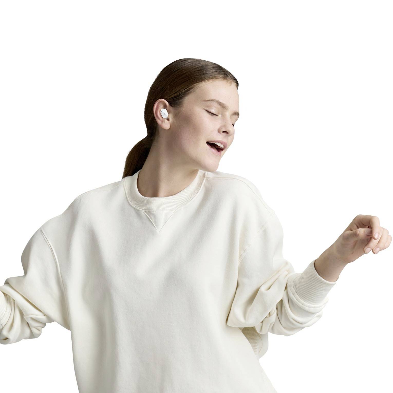 Frau in weißem Pullover hört Musik mit kabellosen Ohrhörern. Sie lächelt und wirkt entspannt.