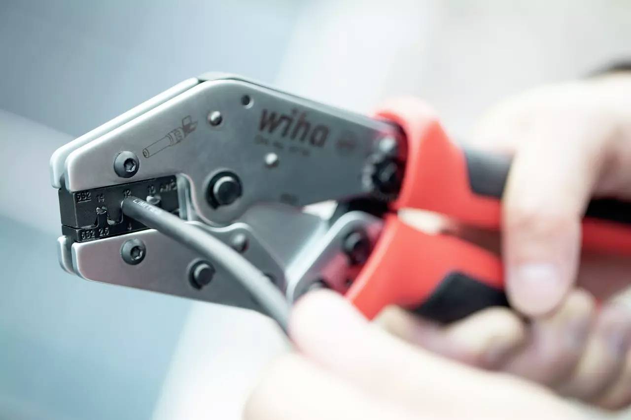 Eine Person benutzt eine rote Crimpzange, um ein Kabel zu bearbeiten. Die Zange wird nah gezeigt und fokussiert den Arbeitsprozess.